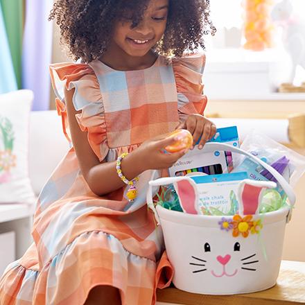 child sitting in dress next to filled Kids Easter basket