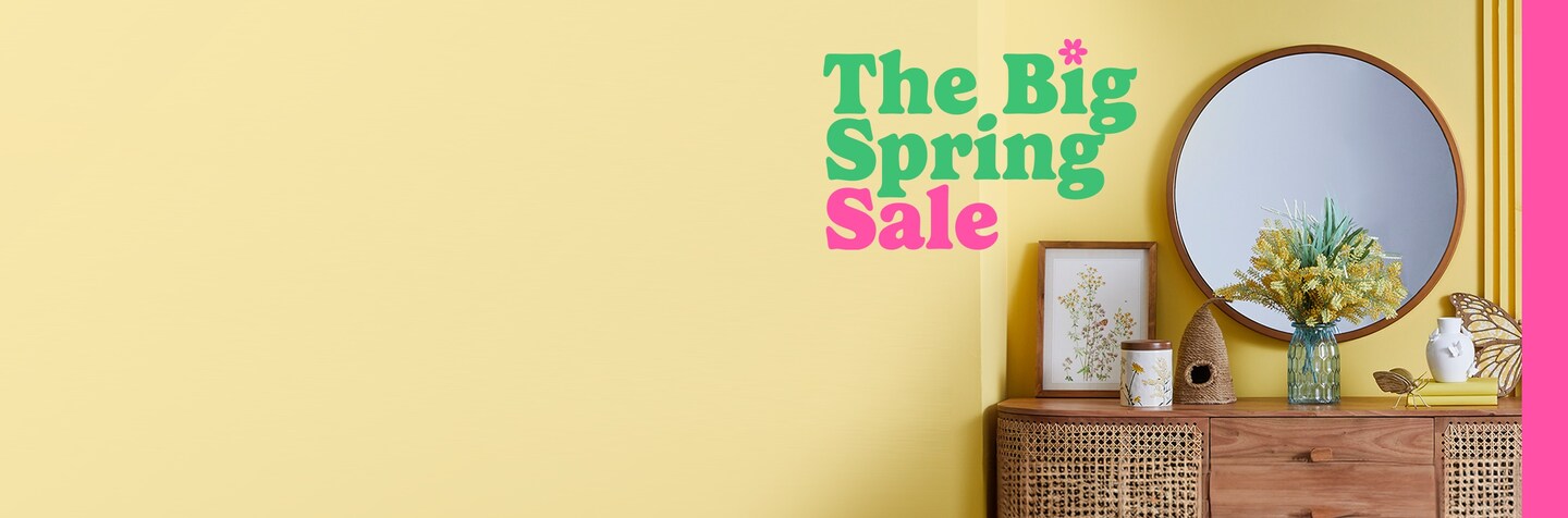 The Big Spring Sale logo in green and pink on yellow wall with natural wood mirror and chest