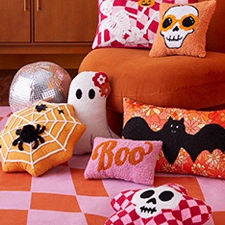 Orange and pink pillows with bat and skeleton designs and a ghost shaped pillow