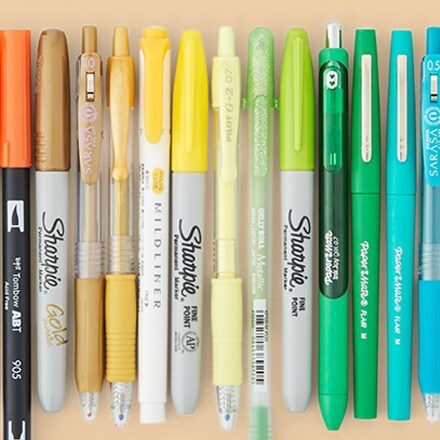 orange, yellow and green markers and pens in a row