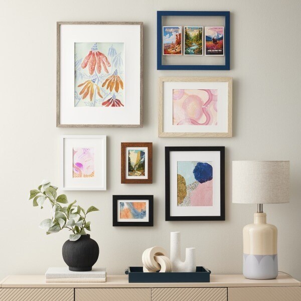 Black, white, brown and navy frames arranged in a gallery wall on a neutral background