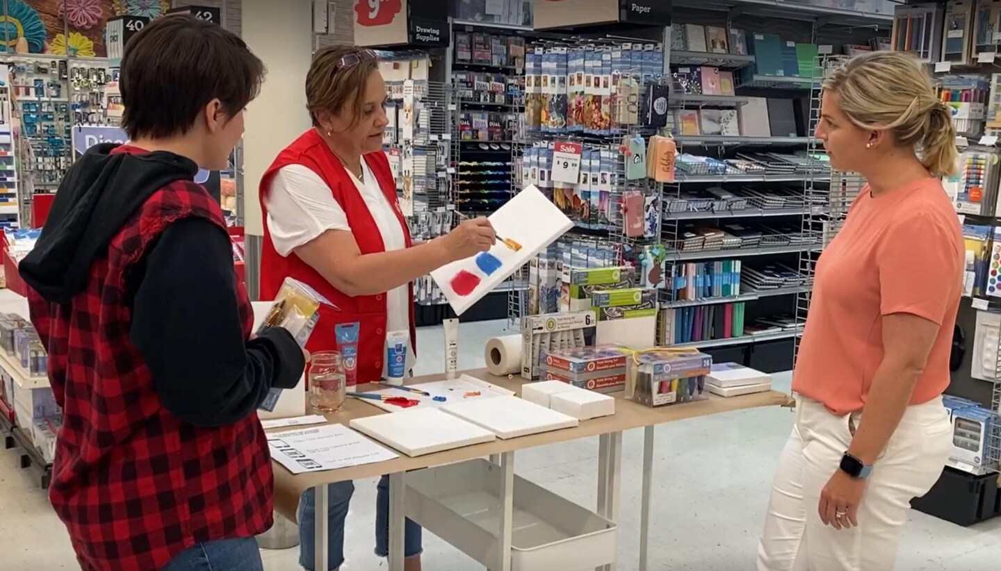 A Michaels employee demonstrates how to paint in front of two store customers