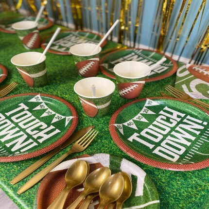 Makerplace by michaels Football-themed tailgate table with turf, field-marked plates, football cups, gold utensils, and striped backdrop creating a festive mood.