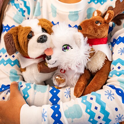 Child holding 3 plushes- a dog, artic fox, and reindeer. 