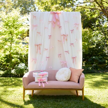 pink couch with pillows in front of white curtain background with pink ribbon bows