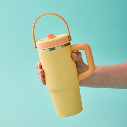 hand holding yellow tumbler with handle on blue background