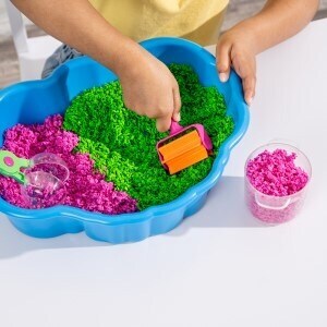 Purple and green sensory sand in a blue bin. A child is rolling out the sand in the bin. 