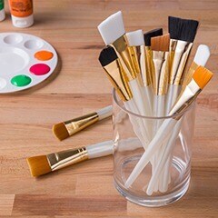 paint brushes in a glass on a wooden tabletop with a paint tray