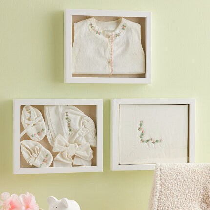three white shadow boxes on wall with baby clothes and blanket inside