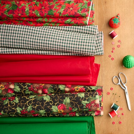 red, green and poinsettia fabric cuts on wood table with sewing supplies