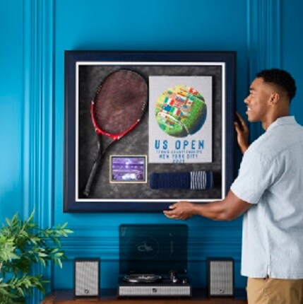 man hanging framed racket with tennis memorabilia 