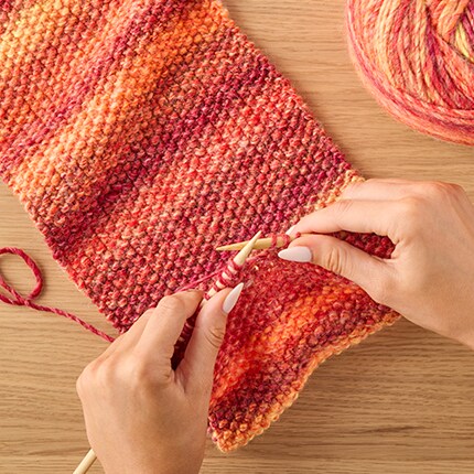 hands knitting and scarf in different shades of orange and red