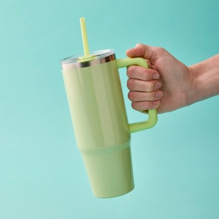 hand holding green tumbler on blue background