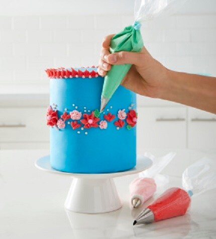 Main tenant une poche à douille décorant un gâteau bleu avec un glaçage en forme de fleur rouge.