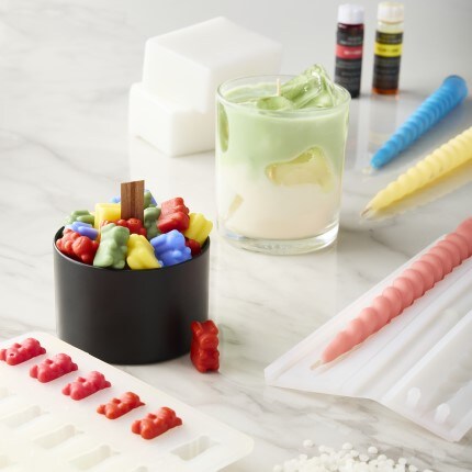 DIY candle making supplies with gummy bear and swirl molds, wax beads, green wipped wax candle, and assorted colored of swirl candles and gummy bear candles 