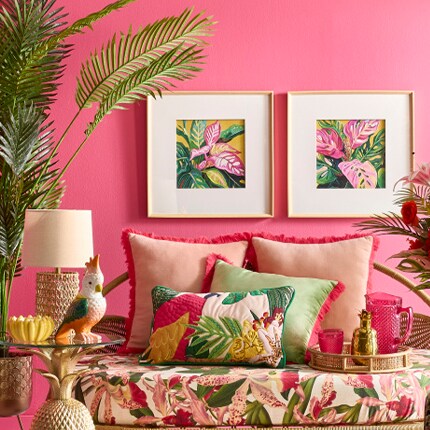 pink tropical pillows and wall art on bright pink wall with greenery
