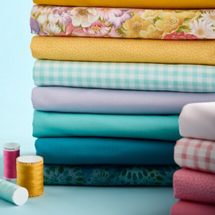 stacks of blu, yellow, pink color fabric and spools of thread