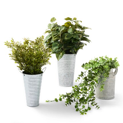 Three artificial green plants in galvanized metal pots arranged on a white background. 