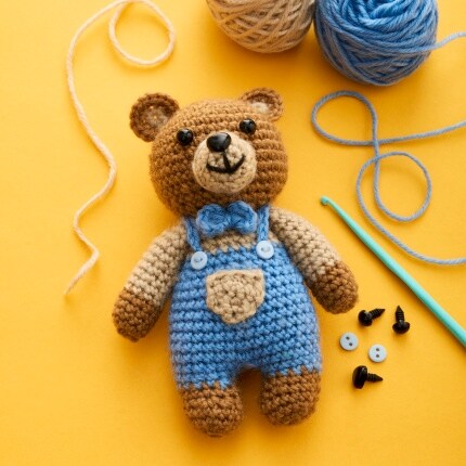 crochet teddy bear wearing overalls on yellow background