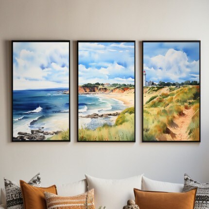 MakerPlace by Michaels Three framed coastal paintings show blue ocean waves, sandy beaches, grassy dunes, and a lighthouse above a sofa with warm pillows.