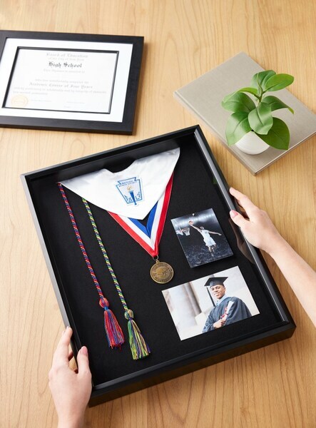 A shadow box with graduation apparel and a diploma in a frame above it.