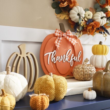 Give Thanks decor collection: tabletop decorative pumpkins in yellow, orange and white colors with a fall floral wreath in the back wall.