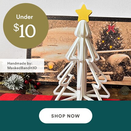 MakerPlace by Michaels 3D-printed white Christmas tree with a yellow star on top, set against a holiday backdrop with text “Under $10.” Button reads "Shop Now."
