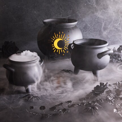 Black cauldrons surrounded by artificial fog and plastic spiders, creating a spooky Halloween atmosphere.