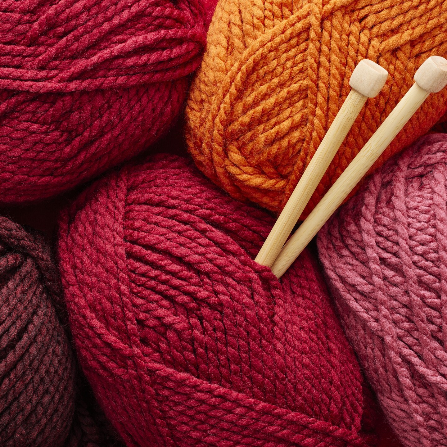 bundle of red toned yarn with wooden knitting needles