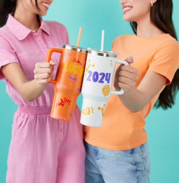 Two women holding tumblers together with 2024 painted on them.