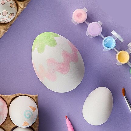 Eggs with painted and a set of paint pots next to it. Over a purple background. 