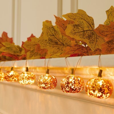 orange pumpkin string lights hanging on white fireplace with fall leaf garland