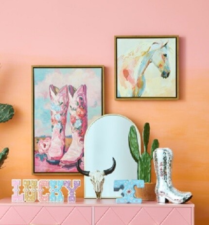 painting of pink boots and horse painting on orange wall above arched mirror and western table accents