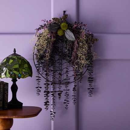 Decorative wreath, featuring dark green leaves, purple flowers, yellow-green moss, and butterfly accents. 