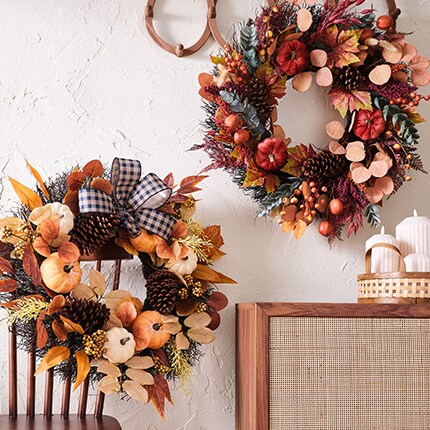 Floral wreath with orange and red leaves, orange pumpkins and a striped red and black bow.