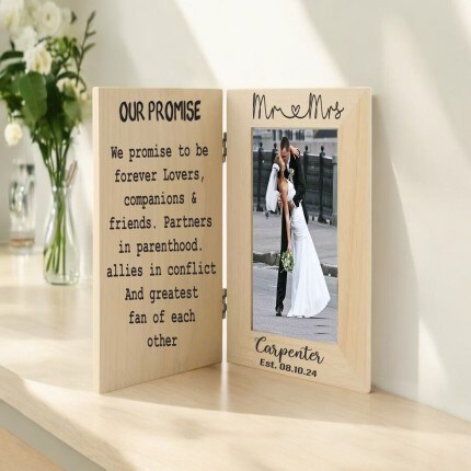 MakerPlace by Michaels A wooden hinged frame on a table displays wedding vows on one side and a photo of a couple kissing on the other. Romantic tone with flowers in the background.