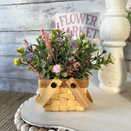 MakerPlace by Michaels A natural basket with floral arrangements over a tabletop. A sign behind that says "Flower Market" in purple font.