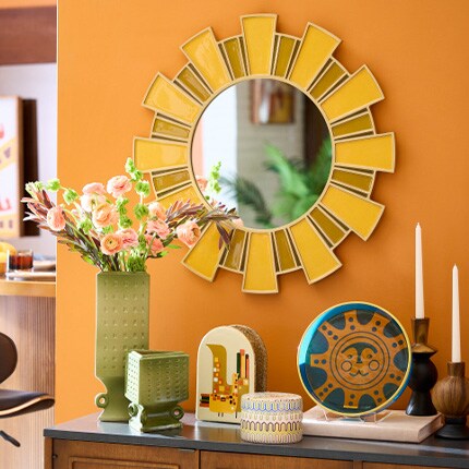 sun burst mirror on orange wall and boho table accents, vases and candle holders