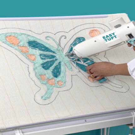 hand using rug tuft gun with light blue yarn on canvas with butterfly design