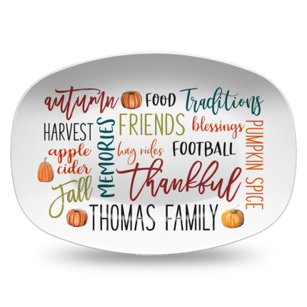 MakerPlace by Michaels White plate with autumn-themed words like "thankful," "friends," and "pumpkin spice" in colorful fonts. Two small pumpkins add a fall touch.
