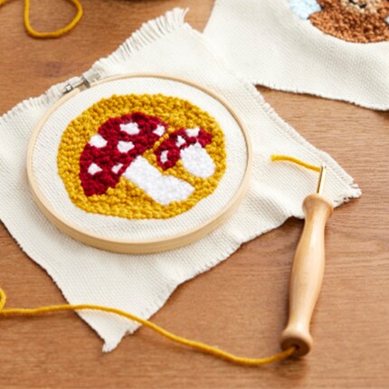 Conception de champignon en punch needle dans un tambour avec fil et outil à aiguille.