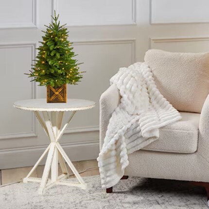 A small Christmas tree in a pot next to a white chair