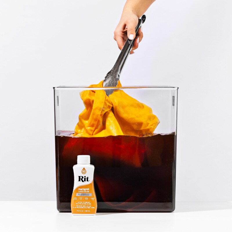 tongs pulling yellow fabric out of dye bucket with fabric dye bottle