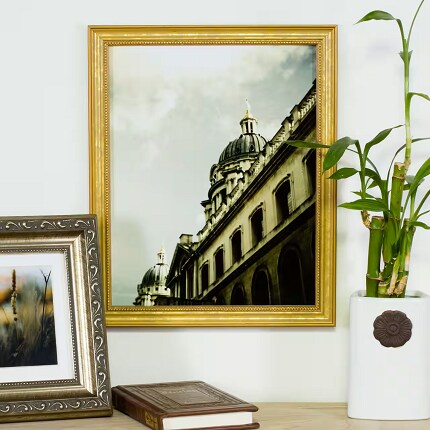 gold frame with photo of building above table with frame, book and plant
