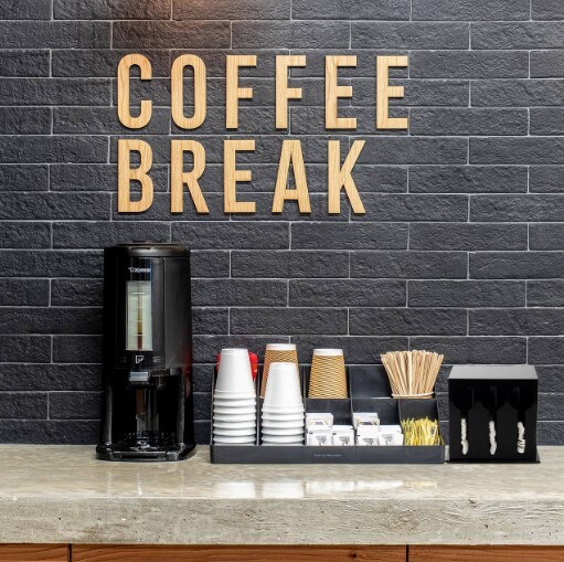 A coffee station with a coffee pot and an organization cubby with cups, coffee sleeves, stirrers, and sugar. 