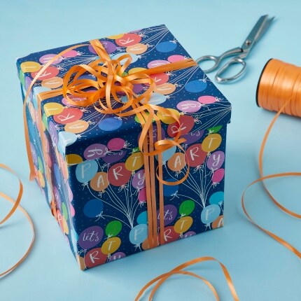 gift wrapped present with orange curling ribbon and scissors on blue table