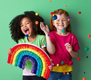 Two children throwing poms poms holding a rainbow made of poms poms