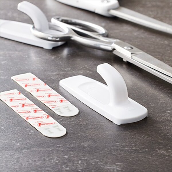 A pair of scissors, hooks, and adhesives lying on a surface.