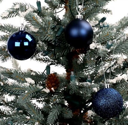 three navy ball ornaments in different finishes hanging from Christmas tree 