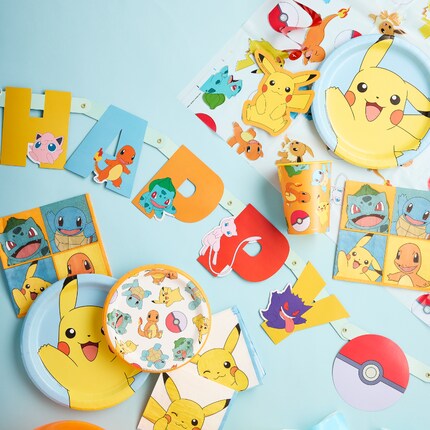A colorful Pokémon-themed party table features a cake with Pikachu topper, surrounded by character plates, cups, blue forks, and vibrant balloons above.